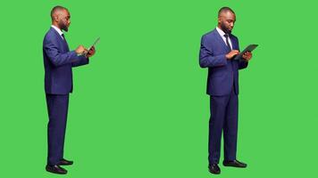 Modern employee browsing internet website on tablet, working with online network page over full body green screen backdrop. Young adult in office suit holding gadget in studio. photo