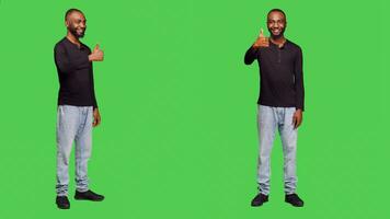 Cheerful adult showing thumbs up gesture on camera, expressing approval and like symbol. Young smiling man doing okay agreement sign, feeling happy about success over green screen. photo