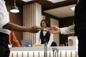 Guest giving cash to bellboy in lobby, paying money for luxury service to carry luggage and suitcases. Hotel concierge receiving payment from tourist, helping with trolley bags. Close up. photo