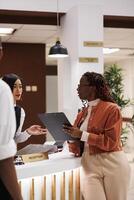 Young woman doing check in process for room registration at luxury hotel, using tablet to fill in forms for booking record. Tourist arriving at reception desk in lobby, accommodation. photo