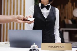 Front desk staff giving key card to man, helping to gain access to hotel room with cardkey reader. Tourist filling in registration forms and doing check in at reception counter. Close up. photo