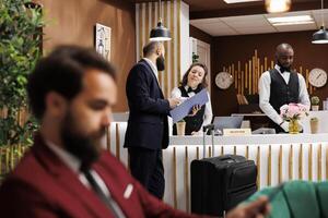 Hotel concierge assisting client at front desk, working on check in procedure to help businessman with accomodation. Traveller signing forms for booking registration, international conferences. photo