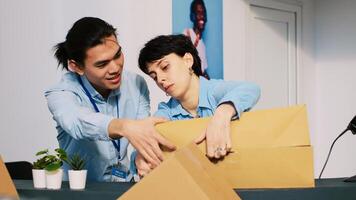 Diverse fashion store workers preparing online orders, putting fashionable merchandise in cardboard boxes. Stylish employees discussing customers shipping details in modern boutique. photo