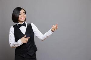 Smiling asian waitress wearing uniform pretending to play guitar while having fun and relaxing. Cheerful woman receptionist imagining to hold musical instrument and expressing happiness photo