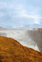 Gullfoss cascade in Iceland, consists of majestic river stream and untouched arctic nature. Nordic scenic route with huge waterfall and stream flowing alongside snow covered hills. photo