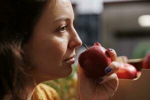 Woman smelling organic farm grown apples in zero waste store with low carbon footprint. Client testing to see if local neighborhood shop fruits are fresh and pesticides free, close up photo