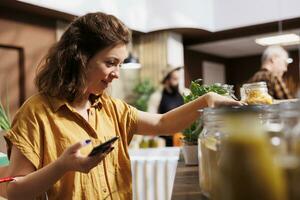 Healthy living woman on a diet using smartphone to make sure zero waste supermarket food is suitable for her. Customer in local neighborhood bio store making sure products are organic photo