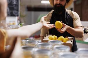 Customer in zero waste supermarket talking with shopkeeper, inquiring about freshly received batch of farm grown organic fruits. Environmentally mindful client in eco store asking for healthy products photo