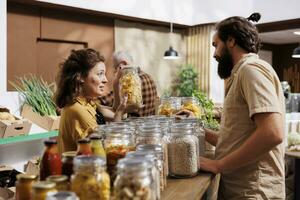 Farmer showcasing her products in zero waste marketplace location, selling chemicals free food to interested buyer. Local trader selling organic farm grown bulk products during event to client photo