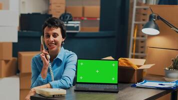 Female worker answering telephone with cord at desk using greenscreen laptop, using chromakey isolated display. Business owner planning shipment on landline phone call with mockup. photo