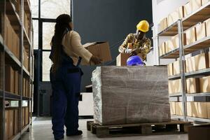 Package handler bringing parcels to warehouse worker for packing. African american storehouse employees sealing cardboard boxes with goods and preparing clients orders for dispatching photo