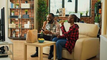 Life partners preparing to eat food from takeout bag, receiving delivery order before binge watching tv show in living room. Young people eating fast food meal for dinner, film on television. photo