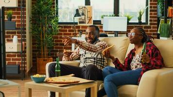 Happy couple eating slices of pizza at television, feeling relaxed watching movie together. Young life partners laughing and eating fast food delivery meal in living room, having fun. photo