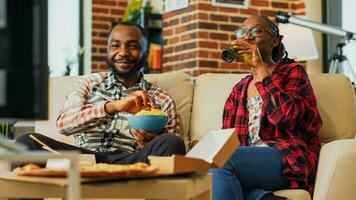 Young couple ordering takeaway food at home to watch television together, feeling relaxed with action film and bottles of beer. Man and woman laughing at tv show. Handheld shot. photo