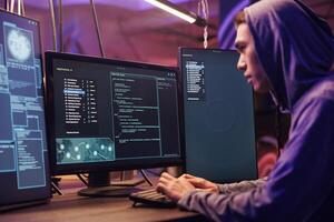 Asian hacker using ransomware to attack server and cracking password. Internet scammer in hood planning phishing attack and developing malicious software to breach data in dark room photo