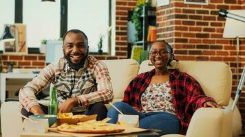 Happy couple laughing at comedy movie on television, feeling cheerful spending time together. Young man and woman enjoying film on tv, eating snacks and delivery food. Tripod shot. photo