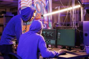 Two hackers in hoods breaking into network system and accessing dark web. Young cybercriminals cracking server password and searching for confidential information to steal photo