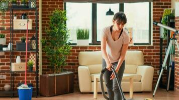 Housewife using vacuum cleaner to tidy up living room, cleaning dust and debris in apartment space. Young adult doing spring cleaning weekend activity, vacuuming wooden floors. photo