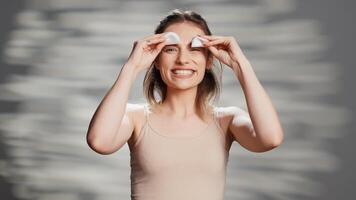 Beauty model acting silly with cotton pads over eyes, playing around in front of camera. Cheerful glowing woman having fun laughing in studio, posing with luminous radiant skin. photo