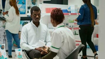 africano americano personas hablando acerca de medicamentos en farmacia, hablando acerca de atención a la salud con vitaminas y drogas farmacia dando caja de suplementos y pastillas a cliente en salud centro. foto