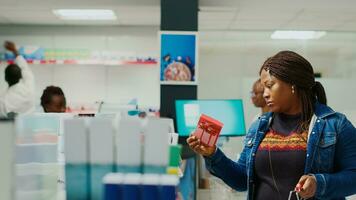 Woman taking medicaments off of drugstore shelves, looking at medical products to buy prescription medicine. Young customer checking leaflets of supplements and pills, retail store. photo