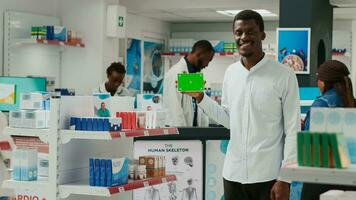 Male client holding box of pills with greenscreen in drugstore, showing isolated mockup template on drugs packages. Young man using blank chromakey copyspace in healthcare shop. photo