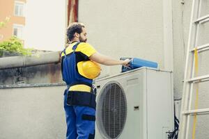 Qualified technician contracted to fix outdoor air conditioner starting job shift. Proficient engineer wearing protective gear preparing to fix damaged external hvac system photo