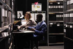 Diverse employees analyzing depository documents, working at administrative report in arhive room. Businesspeople discovering information about bureaucracy record in corporate repository photo