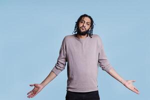 Puzzled arab man with hands spread in questioning gesture looking at camera and making unsure facial expression. Confused thoughtful person shrugging shoulders portrait photo