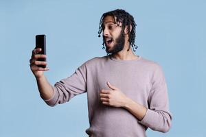 Arab man talking on video call using smartphone front camera. Young person speaking, holding mobile phone while having online communication in videoconference meeting app photo