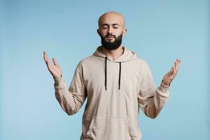 árabe hombre Orando y haciendo Adoración gesto con abierto brazos y cerrado ojos. joven religioso persona alabando, Suplicando a Dios con elevado manos y preguntando para perdón concepto foto