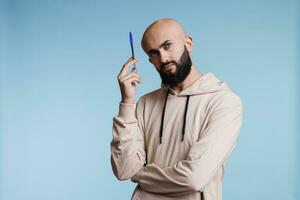 Thoughtful arab man making decision and considering options while holding pen. Pensive young arabian person counting in mind while looking away with puzzled facial expression photo