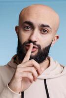 Arab man holding finger on lips while showing silence gesture and looking at camera. Person posing with forefinger on mouth, making quiet sign and asking to keep secret studio portrait photo