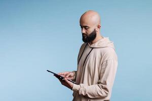 Young concentrated arab man working on digital tablet, typing online message. Focused person reading online on portable electronic gadget, scrolling internet pages and texting photo