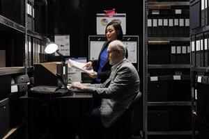 Business invoicing management employees comparing accountancy market data analysis digital paperwork. Archival depository filled with folders in cabinet and graphic charts photo