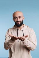 Charming arab man flirting and sending air kiss while looking at camera. Young romantic handsome bald bearded person expressing love and affection with gesture studio portrait photo