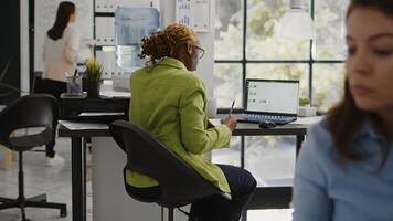 Business woman looking at annual report on laptop, planning corporate investment for marketing development. Startup worker checking data analytics on pc, taking notes on documents. photo