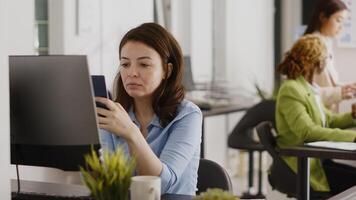 Successful businesswoman taking social media break at desk, checking online website on smartphone app. Young manager using mobile phone and planning project for investment. Handheld shot. photo