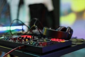 Dj controller with jog wheels, knobs and buttons for electronic music mixing at nightclub stage. Musician console panel and headphones for live performance in club close up photo