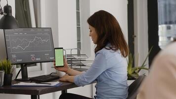 Female entrepreneur looking at greenscreen display on smartphone, working in business office with chroma key template. Young adult analyzing mobile phone screen with isolated copyspace. photo