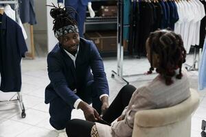 Store employee helping customer with fashionable shoes, woman shopping for casual wear in showroom. African american client buying fashion collection in boutique shop. Fashion concept photo