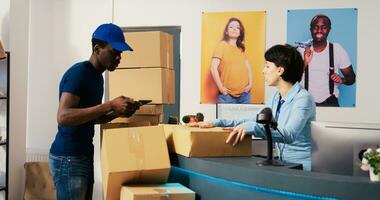 African american deliveryman asking worker to sign distribution report on tablet computer, discussing customer shipping detalis in shopping mall. Employee preparing packages in modern boutique photo
