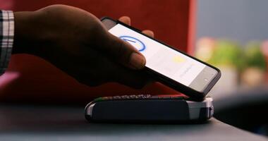 African american customer using phone nfc payment after buying stylish merchandise and accessories in modern boutique. Shopper paying for fashionable casual wear at counter desk. Close up. photo