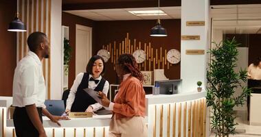 Busy concierge personnel performing various administrative tasks in hotel lobby while guests are being checked in. Tourists booking in their room helped by friendly receptionist and helpful bellboy photo