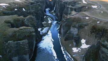 Spectacular fjadrargljufur canyon aerial view with water stream and icelandic scenery, snowy mountains and massive rocks. Majestic nordic landscape with river flowing between hills. Slow motion. photo