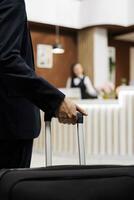 hotel invitado entrando recepción con equipaje, de viaje extranjero a atender importante negocio reuniones empresario que se acerca frente escritorio para cheque en, reserva alojamiento. cerca arriba. foto