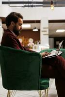 Businessman works on conference speech, waiting in hotel lounge area before attending international board conference with partners. Man in suit preparing for important meeting, work trip. photo