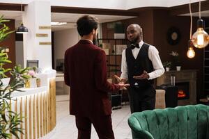 Guest and bellboy discussing in lobby, asking about local recommendations while he is visiting on business trip. White collar worker being greeted by bellhop at hotel, luxury services. photo