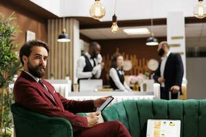 Entrepreneur in suit at hotel, waiting to attend important business meeting with executive board. Formal guest travelling for work, being invited to international conference. Lounge area. photo