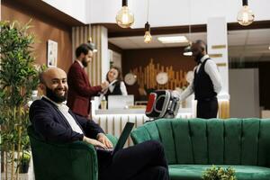 Businessman on laptop in lounge area at hotel, working on conference speech before doing check in process. Luxury resort provides excellent amenities and services to enhance work trip experience. photo